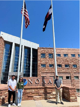 Three people standing in front of a NOAA building